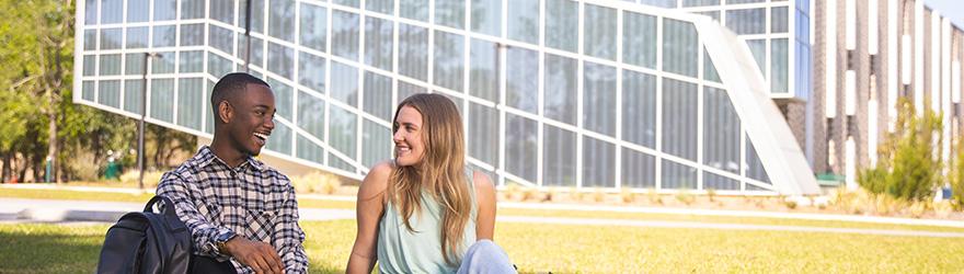 Two students smile while sitting on the lawn of the Lab Sciences Annex.