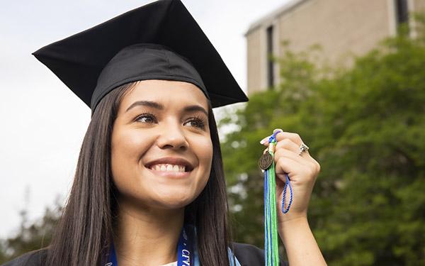 A UWF graduate in cap and gown holds up a tassel.