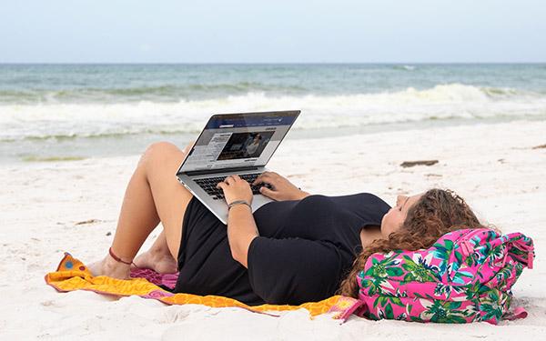 A UWF student uses a laptop while lying on Pensacola Beach.